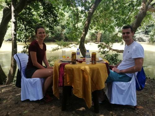 un uomo e una donna seduti a un tavolo di fronte a un fiume di Induwara Safari Resort a Udawalawe