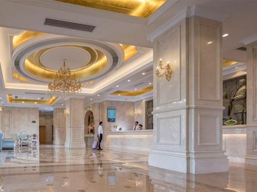 una persona parada en un gran vestíbulo con una lámpara de araña en Vienna Hotel(Shenzhen Shajing Jingjinbaina Branch) en Shenzhen