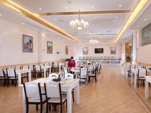 a restaurant with white tables and chairs and a man standing in the middle at Vienna International Hotel (Hunan Changde Taoyuan Longba) in Taoyuan