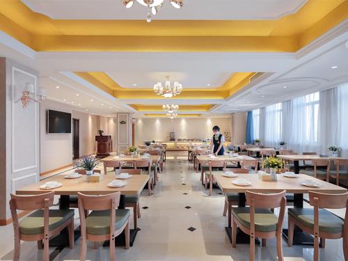 a dining room with tables and a person standing in the background at Vienna Hotel (Dangtu East Railway Station, Ma'anshan, Anhui) in Ma'anshan