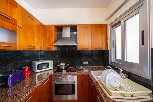 a kitchen with wooden cabinets and a sink and a microwave at Seafront Protaras Apartments in Protaras