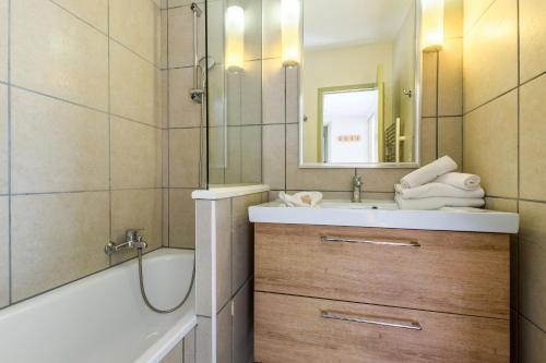 ein Badezimmer mit einem Waschbecken, einer Badewanne und einem Spiegel in der Unterkunft Residence La Foret - maeva Home in Arâches-la-Frasse