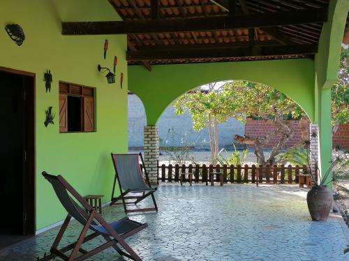 un edificio verde con 2 sillas en un patio en Pousada Flanboyan, en São Miguel do Gostoso