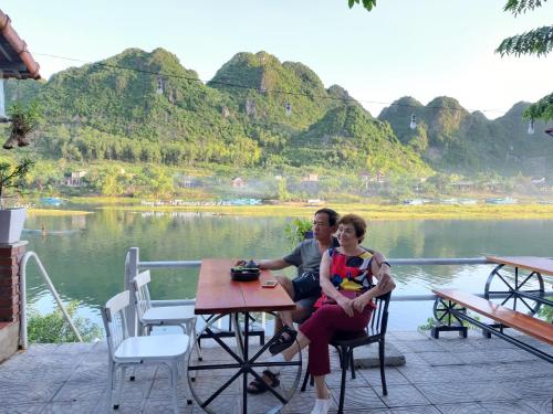 a man and woman sitting at a table near a lake at Areca Bungalow in Phong Nha