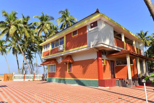a orange building with palm trees in the background at Glucklich Beach Cottages in Kundapur