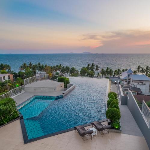 a swimming pool with chairs and the ocean in the background at Exclusive Garden View 1 bedroom suite @Patio Bangsaen in Bangsaen