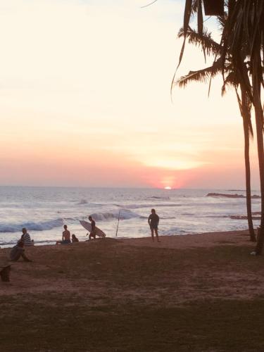 a group of people sitting on the beach at sunset at Naomi Beach Resort - Adults only in Weligama