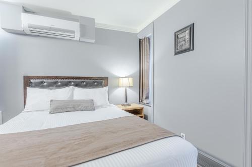a white bedroom with a bed and a air conditioner at Hotel Jardin du Gouverneur in Quebec City
