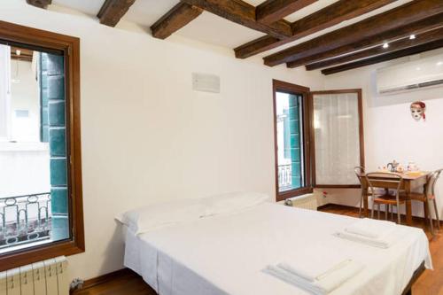 a white bed in a room with a table and windows at Studio in San Marco square in Venice