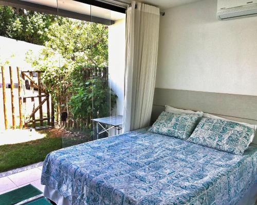 a bedroom with a bed with a blue comforter and a window at Flat Village Imbassai Solaris in Imbassai