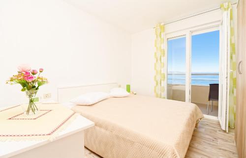 a white bedroom with a bed with a vase of flowers at Apartman More&Maslina in Drasnice