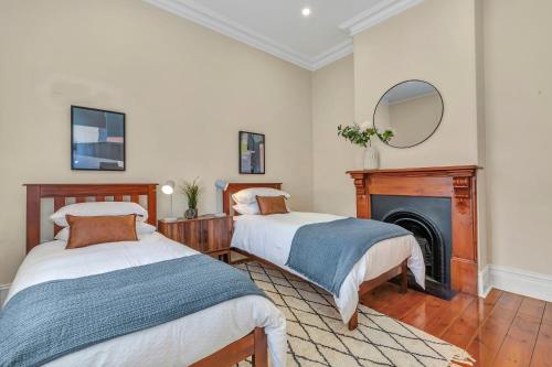 two beds in a room with a fireplace and a mirror at The Barton - Easy Tram to City in Thebarton