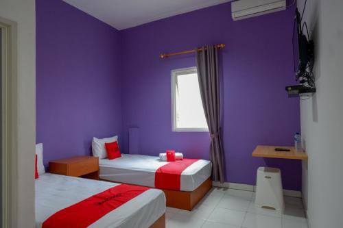 a purple bedroom with two beds and a window at RedDoorz near Alun Alun Kaliwungu Kendal in Brangsong