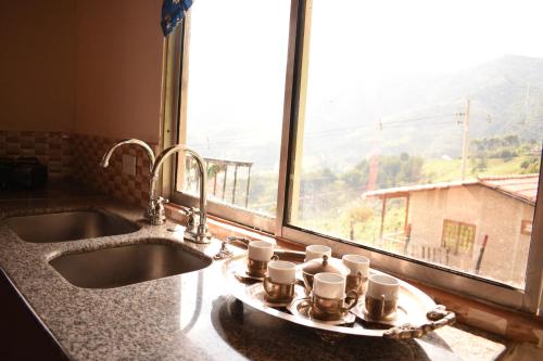 ein Waschbecken mit Kaffeetassen auf einem Tablett neben einem Fenster in der Unterkunft Casa de Campo con hermosa vista a Los Farallones in Versalles