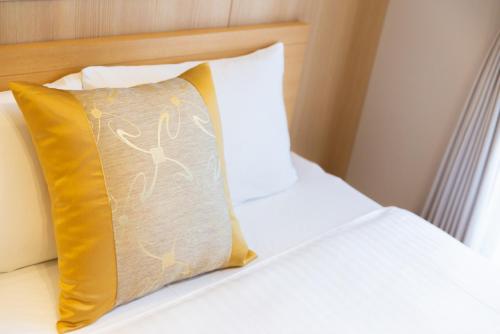 a white bed with a yellow pillow on it at GRAND BASE Hiroshima Hikarimachi in Hiroshima