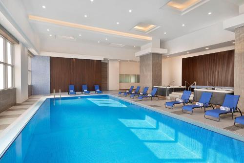 voco Al Khobar, an IHG Hotel في الخبر: مسبح كبير والكراسي الزرقاء في غرفة الفندق