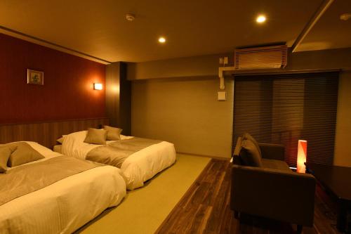 a hotel room with two beds and a chair at Hotel Imari Aioibashi Bettei in Imari