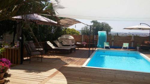 a swimming pool with chairs and an umbrella at צימר בגליל אביב בבקתה in Galilee