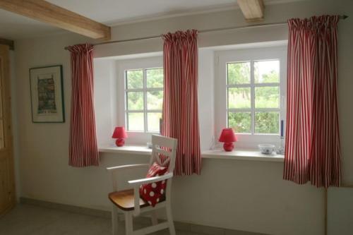 a room with red curtains and a chair in front of a window at Ferienhaus Deichgraf in Vollerwiek