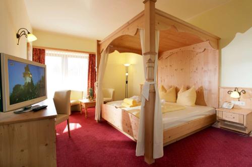 ein Schlafzimmer mit einem Himmelbett und einem TV in der Unterkunft Alpenhof Brixen in Brixen im Thale