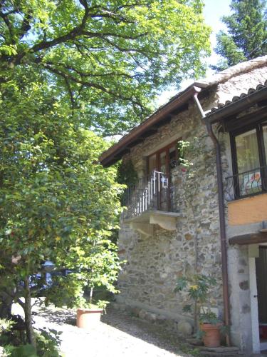 a stone house with a balcony and a tree at Camping & Resort Valle Romantica in Cannobio