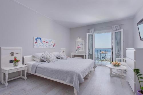 a white bedroom with a bed and a balcony at Adrina Beach Hotel in Panormos Skopelos