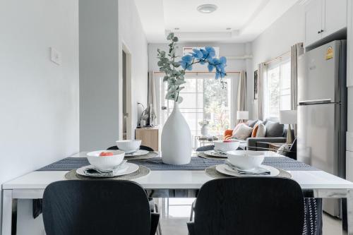 a dining room table with chairs and a white vase with flowers at Chiang Mai Jasmine Cottage in Chiang Mai