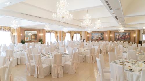 a banquet hall with white tables and chairs and chandeliers at Hotel Villa Romana in Porto Empedocle