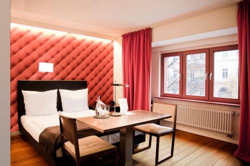 Hotel Adele في برلين: غرفة نوم مع سرير وطاولة مع اللوح الأمامي الأحمر
