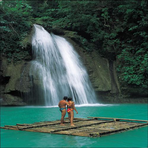 two people standing on a raft in the water near a waterfall at Badian Island Wellness Resort in Badian