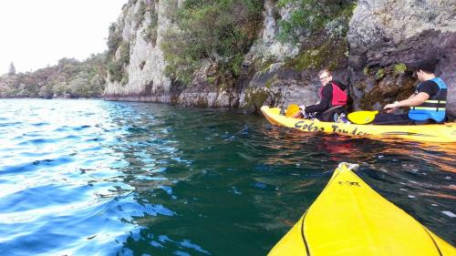 two people on kayaks in the water near a cliff at Tongariro Adventures The Lodge in Kuratau