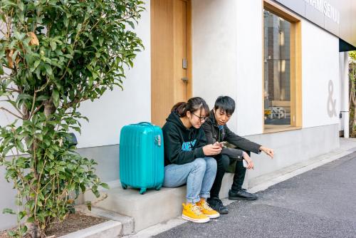 two people sitting on the curb with a suitcase at &AND HOSTEL MINAMISENJU in Tokyo