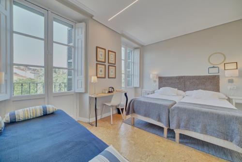 a bedroom with two beds and a desk and windows at Pensión Mendi in Pamplona