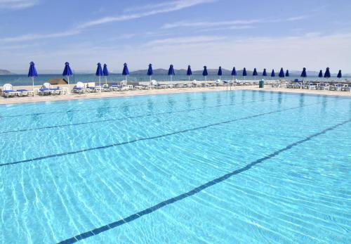 a large swimming pool next to a beach with umbrellas at Mastichari Bay Hotel in Mastichari