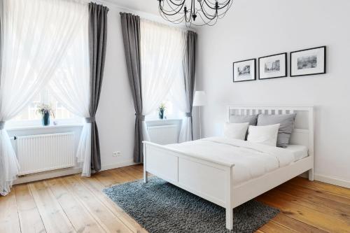 a white bedroom with a white bed and two windows at Apartament Nowe Miasto - przy Parku Róż in Gorzów Wielkopolski