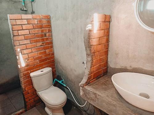 a bathroom with a brick wall and a toilet and a sink at Ozone Beach Huts in Ko Lanta