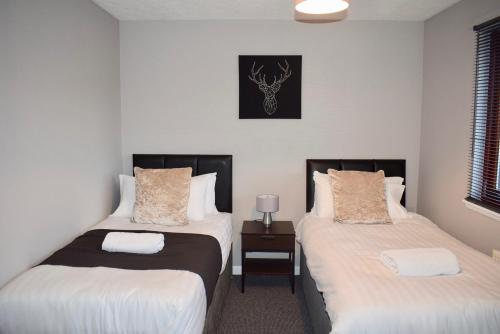 1 dormitorio con 2 camas y mesa con lámpara en Kelpies Serviced Apartments Hamilton- 2 Bedrooms, en Falkirk