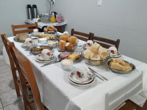 een tafel vol voedsel op een witte tafeldoek bij PÉROLA SUÍTES - PENHA in Penha
