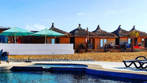 a resort with a pool and tables and umbrellas at Greenwave Ecolodge in Mirleft