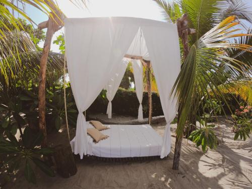 a white canopy bed on a beach with palm trees at La Playita Beach House in Puerto Escondido