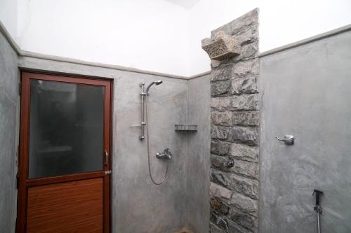 a shower with a wooden door next to a stone wall at Mass Eco Cabana Yoga & Spa - Unawatuna in Unawatuna