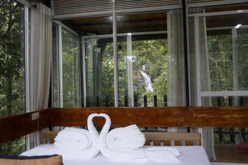 two white swans sitting on a bed in front of a window at Sinharaja Kurulu Ella Eco Resort in Deniyaya