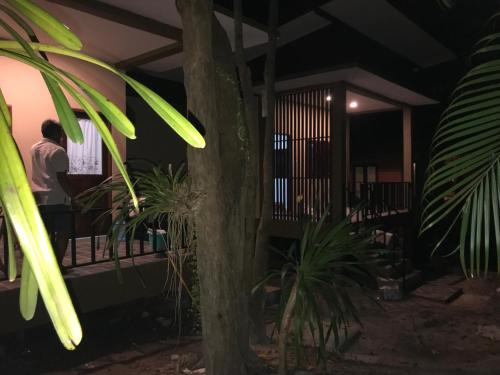 a man standing on a porch at night with plants at Captan Home in Haad Chao Phao