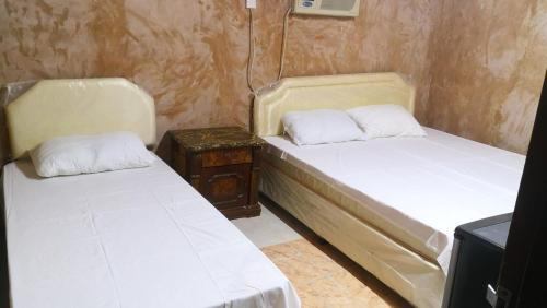 two beds in a small room with a night stand at Bidiya Desert Camp in Aflāj