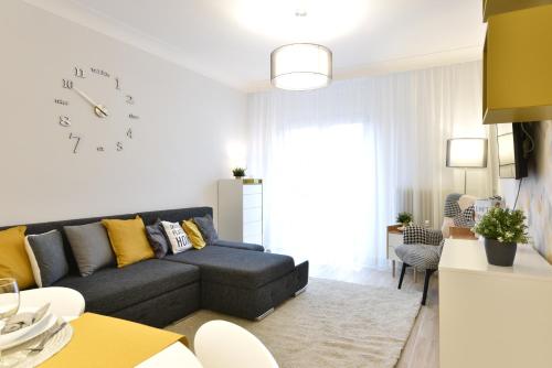 a living room with a couch and a clock on the wall at Királykút 1 apartman - ingyen parkolás, bicajok, ac in Székesfehérvár