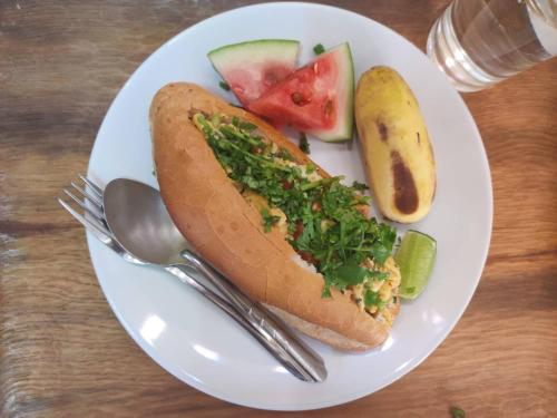 a white plate with a hot dog and a pickle at Bike&Bed in Thakhek