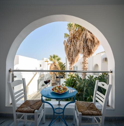 a table with a bowl of fruit on a balcony with palm trees at Alesahne Beach Hotel in Kamari