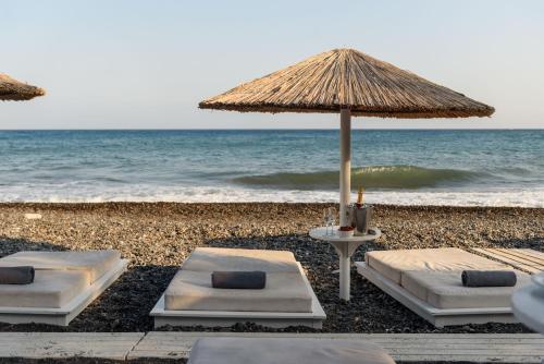 two beds and an umbrella on the beach at Alesahne Beach Hotel in Kamari