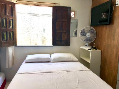 a bedroom with a bed with a window and a fan at Kitnets da vana in Morro de São Paulo