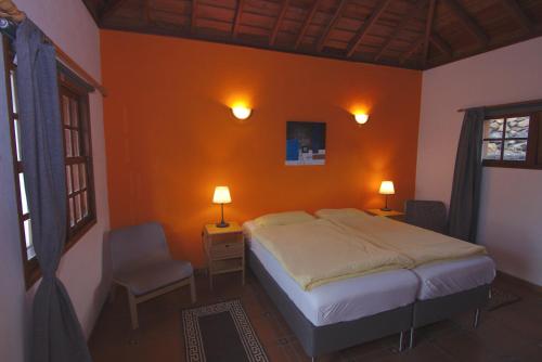 a bedroom with an orange wall with a bed and a chair at Casa Tanausu in Todoque
